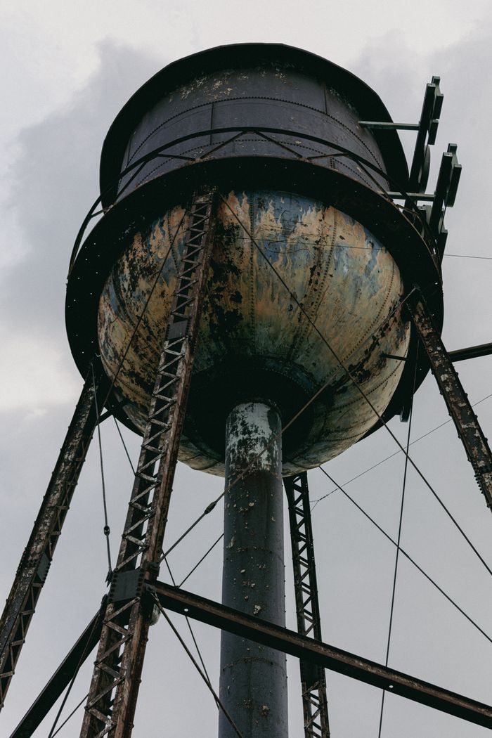 A close-up view of a rustic water tower with peeling paint and a cloudy sky backdrop.