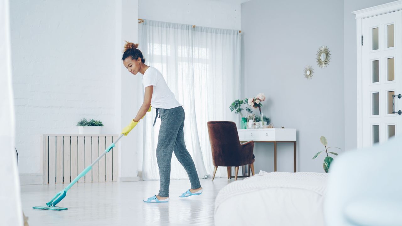 programs-01 A woman cleaning a bright, modern living room with a mop, creating a clean, welcoming space.