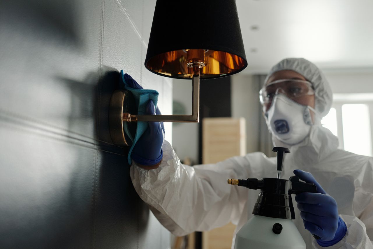 Crafting Captivating Headlines: Your awesome post title goes here A person wearing protective gear sanitizes a wall lamp to prevent virus spread.